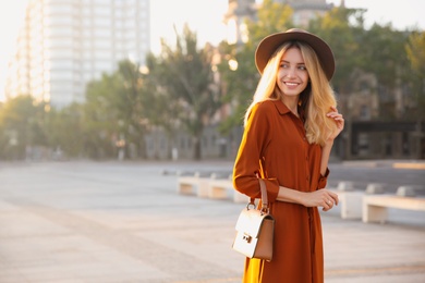 Photo of Beautiful young woman in stylish red dress and hat with handbag on city street