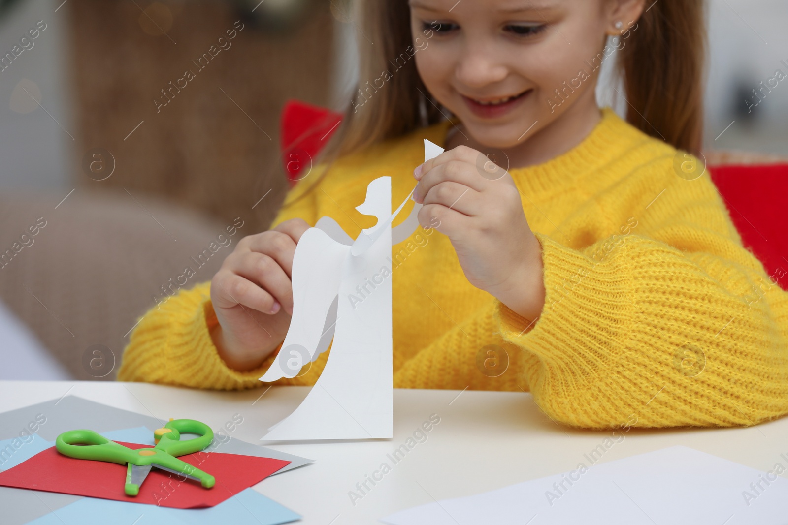 Photo of Cute little girl with paper angel for Saint Nicholas day at home, focus on hands