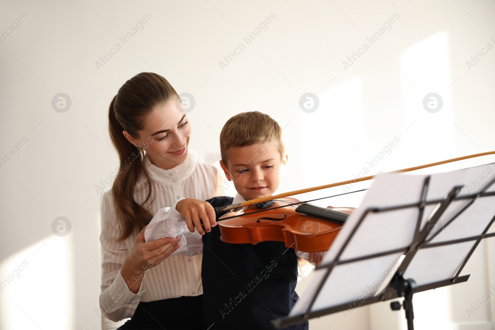 Photo of Young woman teaching little boy to play violin indoors