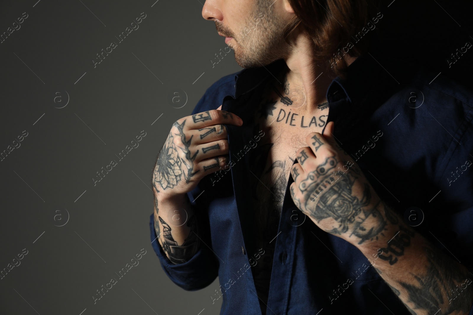 Photo of Young man with tattoos on body against black background, closeup