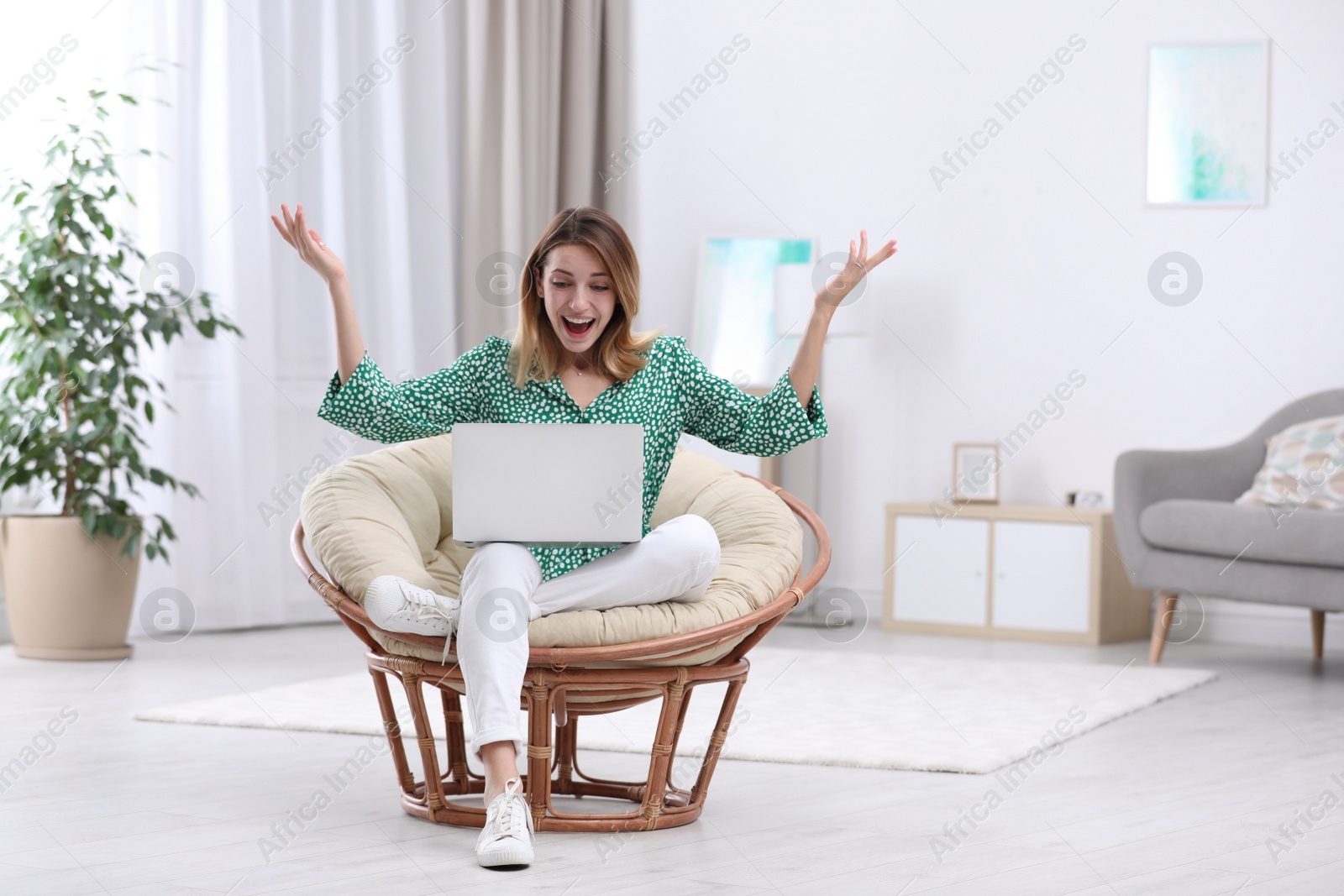 Photo of Emotional young woman with laptop in armchair at home. Space for text