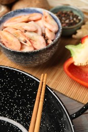 Photo of Black wok, chopsticks and bamboo mat with products on table, closeup