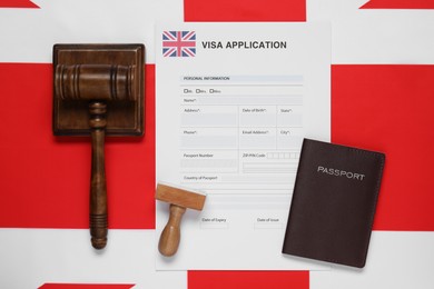 Photo of Immigration to United Kingdom. Visa application form, gavel, stamp and passport on flag, flat lay