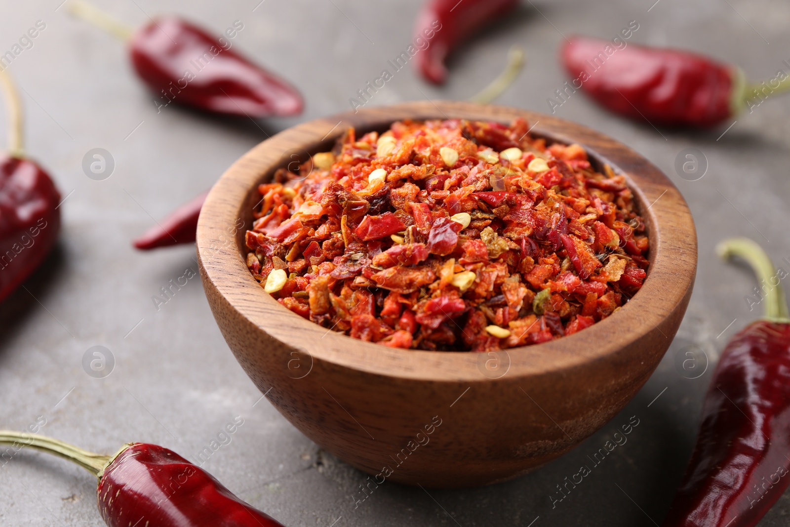 Photo of Chili pepper flakes in bowl and pods on grey table, closeup