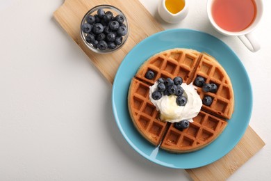 Tasty Belgian waffle with blueberries, honey and whipped cream served on white table, flat lay. Space for text