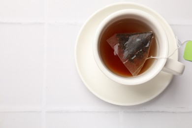 Photo of Tea bag in cup with hot drink on white tiled table, top view. Space for text
