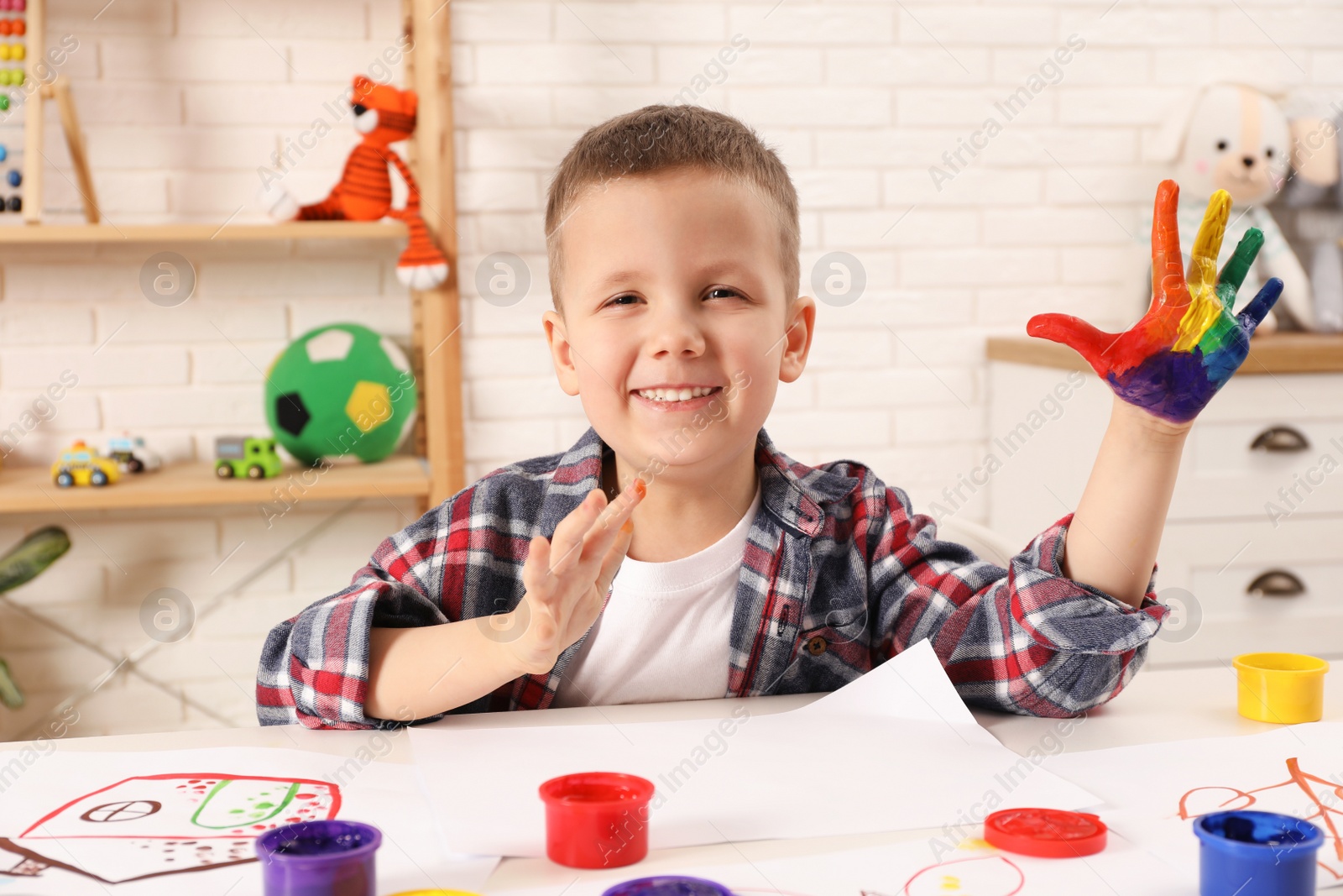 Photo of Happy little boy showing painted palm at white table in room