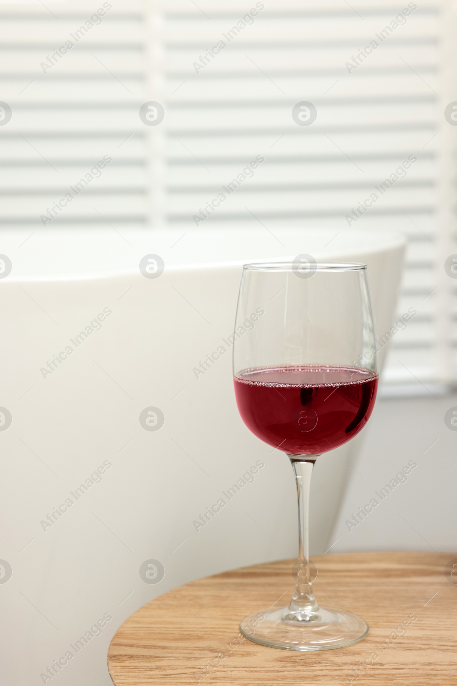 Photo of Glass of red wine on wooden table in bathroom