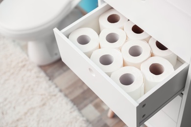 Open cabinet drawer with toilet paper rolls in bathroom