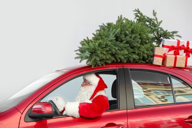 Authentic Santa Claus driving red car with gift boxes and Christmas tree, view from outside