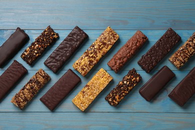 Photo of Different tasty protein bars on light blue wooden table, flat lay