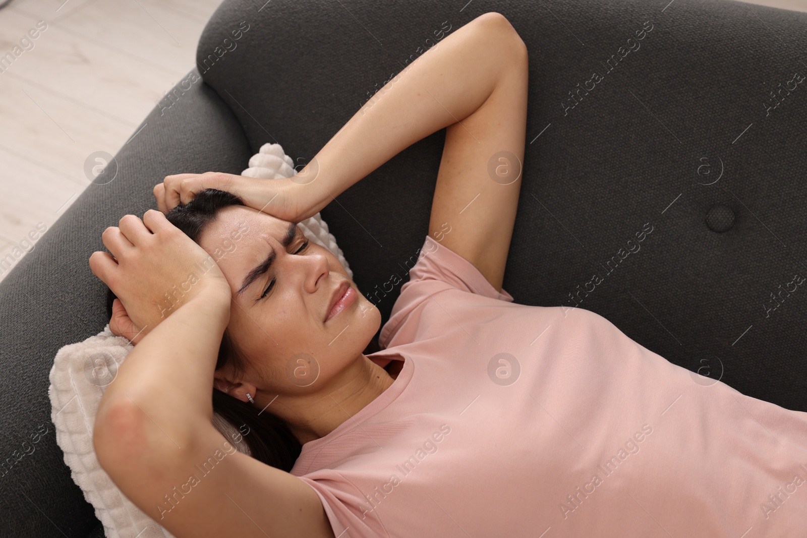 Photo of Sad woman suffering from headache on sofa indoors