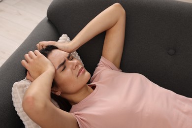Photo of Sad woman suffering from headache on sofa indoors