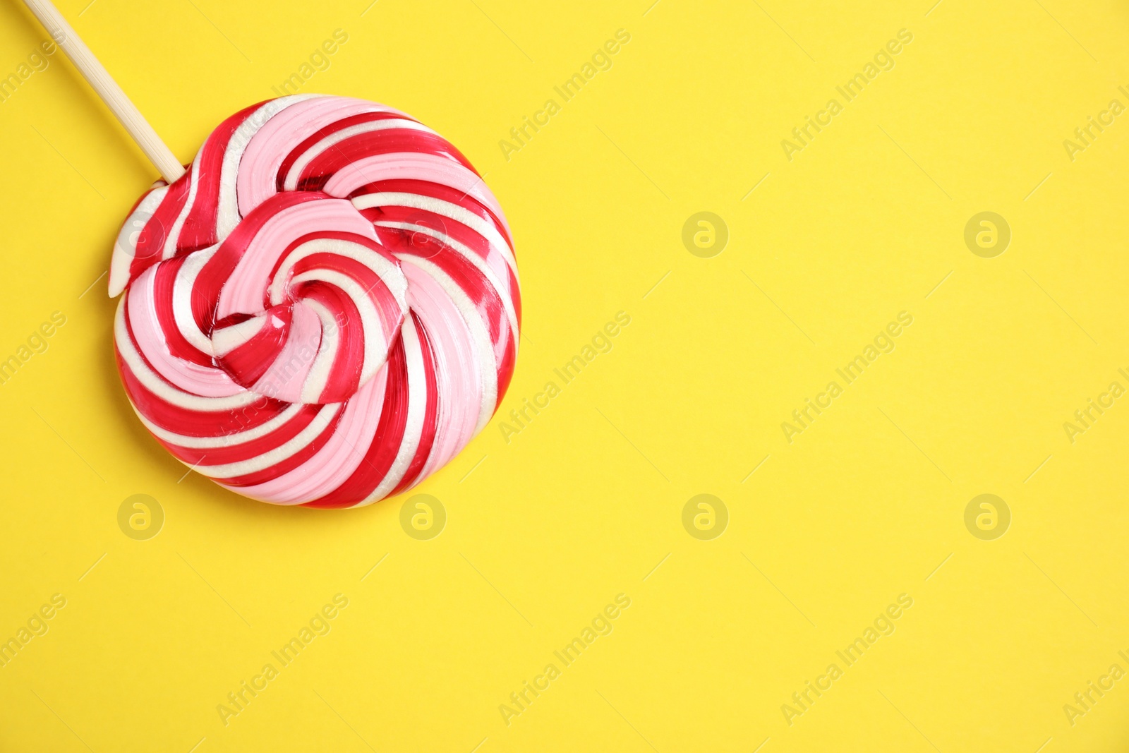 Photo of Stick with colorful lollipop swirl on yellow background, top view. Space for text