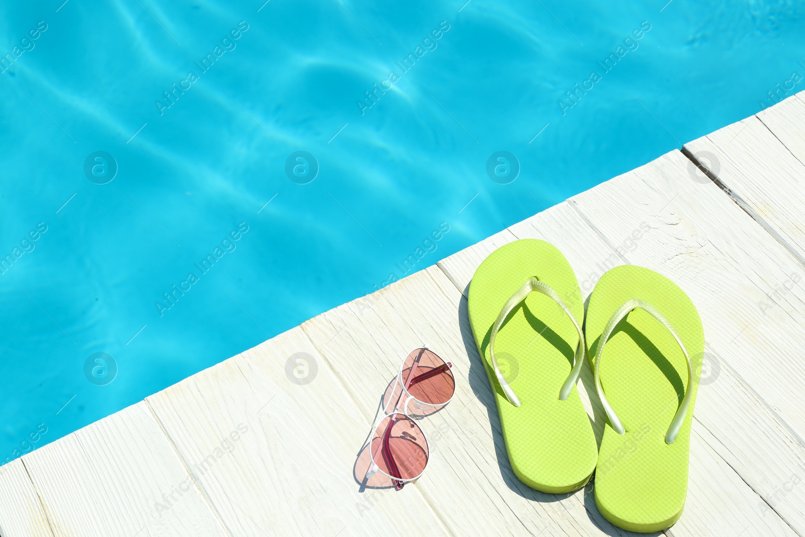 Photo of Slippers and sunglasses on wooden deck near swimming pool, space for text. Beach accessories