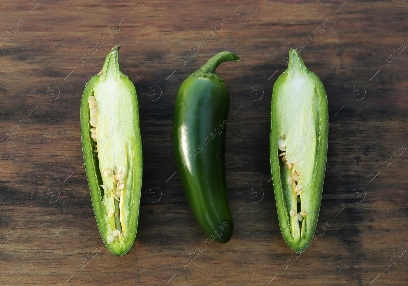 Photo of Whole and cut green chili peppers on wooden table, flat lay