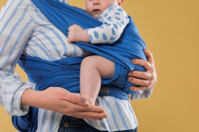 Mother holding her child in sling (baby carrier) on beige background, closeup