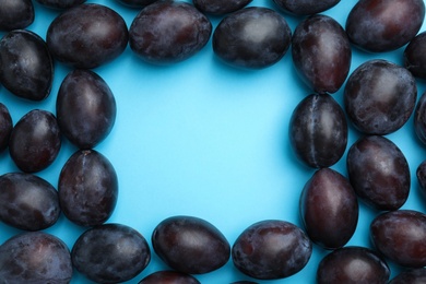 Photo of Frame made of delicious ripe plums on light blue background, flat lay. Space for text