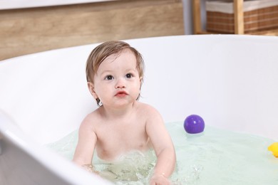 Cute little child bathing in tub at home