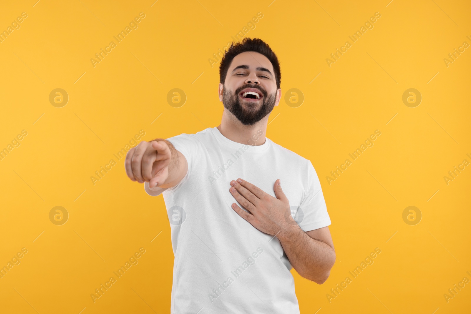 Photo of Handsome young man laughing while pointing at something on yellow background