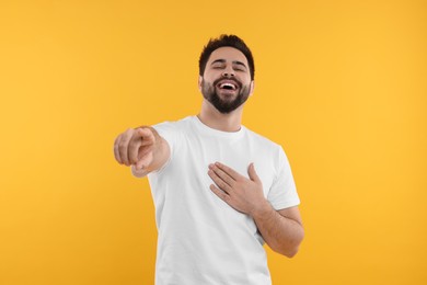 Handsome young man laughing while pointing at something on yellow background