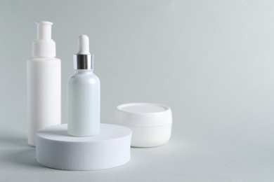 Bottles with cosmetic serums on light grey background, space for text