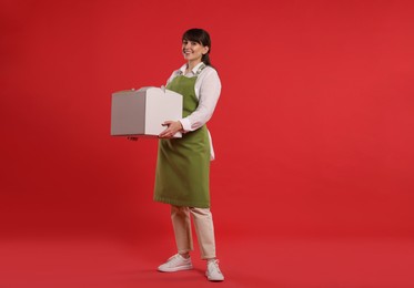 Happy professional confectioner in apron holding cake box on red background