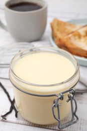 Photo of Tasty condensed milk in jar on white wooden table, closeup