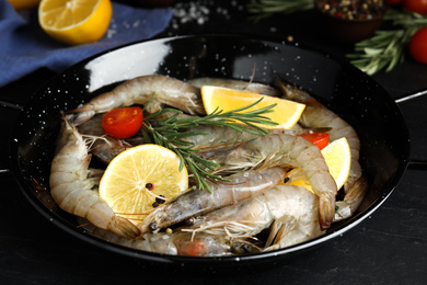 Photo of Fresh raw shrimps with lemon slices on black table
