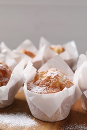 Photo of Delicious muffins with powdered sugar on wooden board, closeup