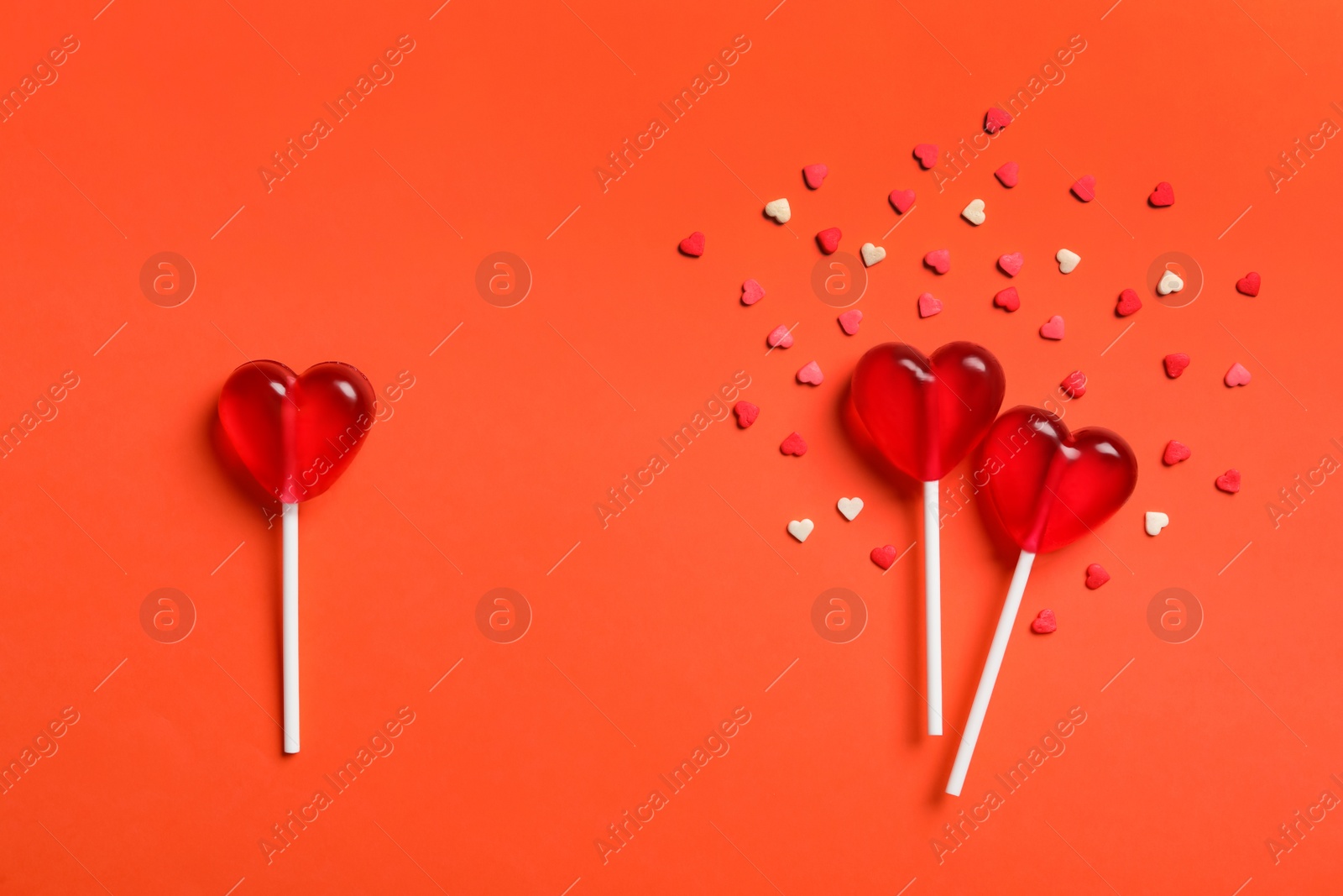 Photo of Flat lay composition with sweet heart shaped lollipops and sprinkles on coral background. Love triangle concept