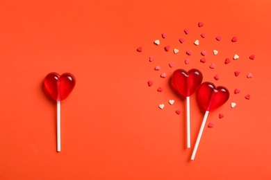 Photo of Flat lay composition with sweet heart shaped lollipops and sprinkles on coral background. Love triangle concept