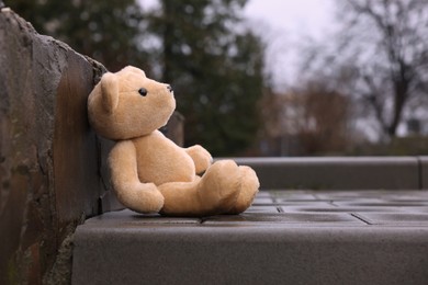 Lonely teddy bear outdoors on pavement near curb, space for text