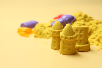 Photo of Castle figures made of yellow kinetic sand on beige background, closeup. Space for text