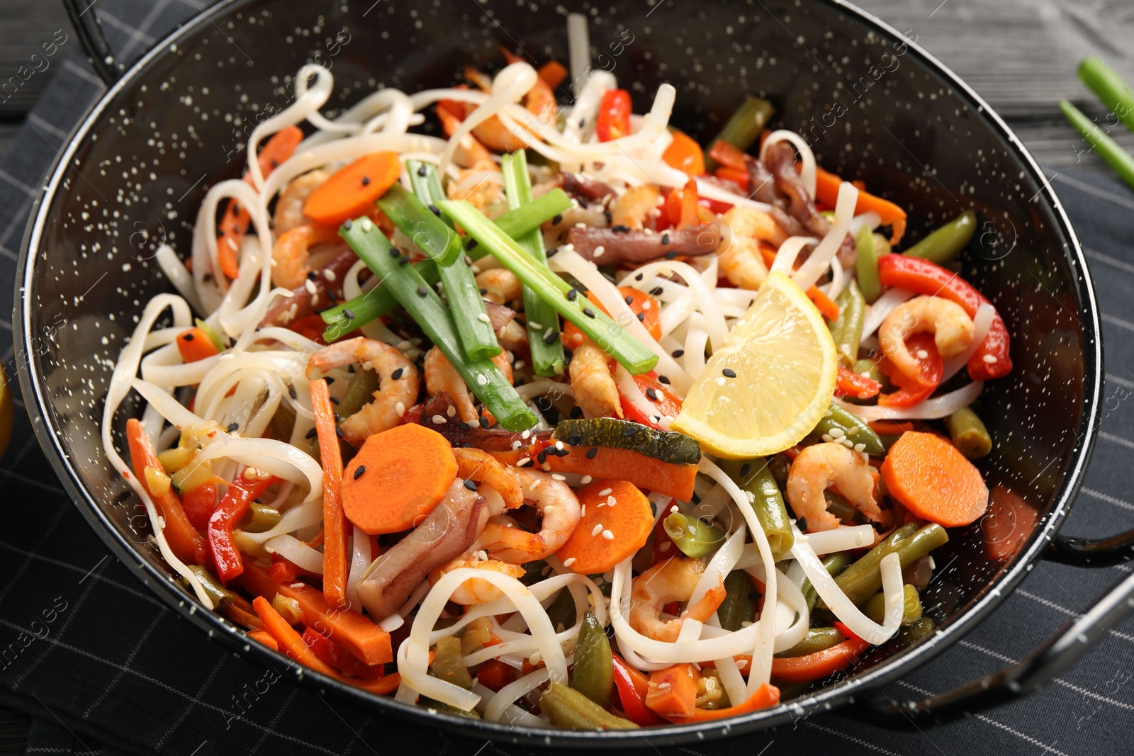 Photo of Shrimp stir fry with noodles and vegetables in wok on black wooden table, closeup