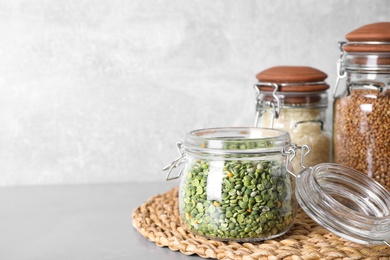 Dry peas, buckwheat and rice in jars on grey table, space for text