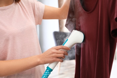 Young woman steaming her clothes at home, closeup