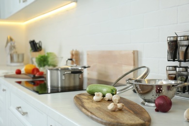 Photo of Fresh vegetables and mushrooms on white countertop in modern kitchen. Space for text