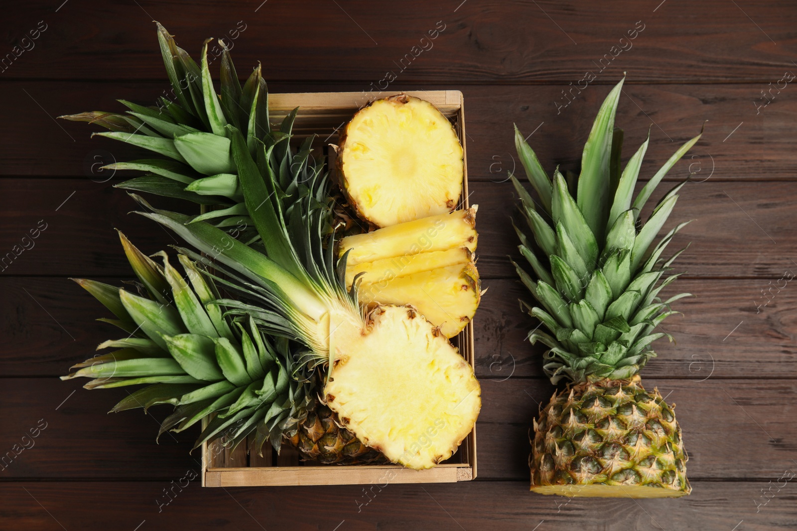 Photo of Tasty cut pineapples in crate on wooden table, flat lay