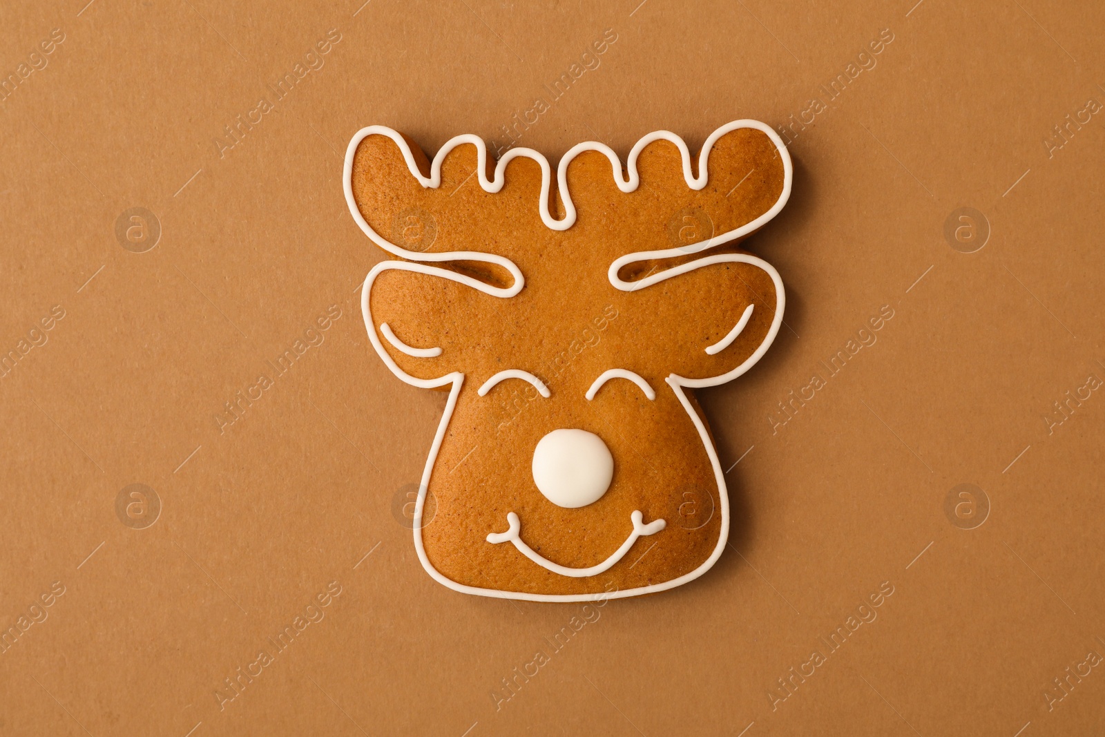 Photo of Christmas deer shaped gingerbread cookie on brown background, top view