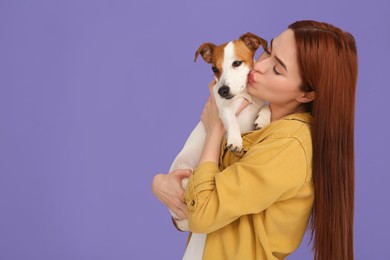Photo of Woman kissing her cute Jack Russell Terrier dog on violet background. Space for text
