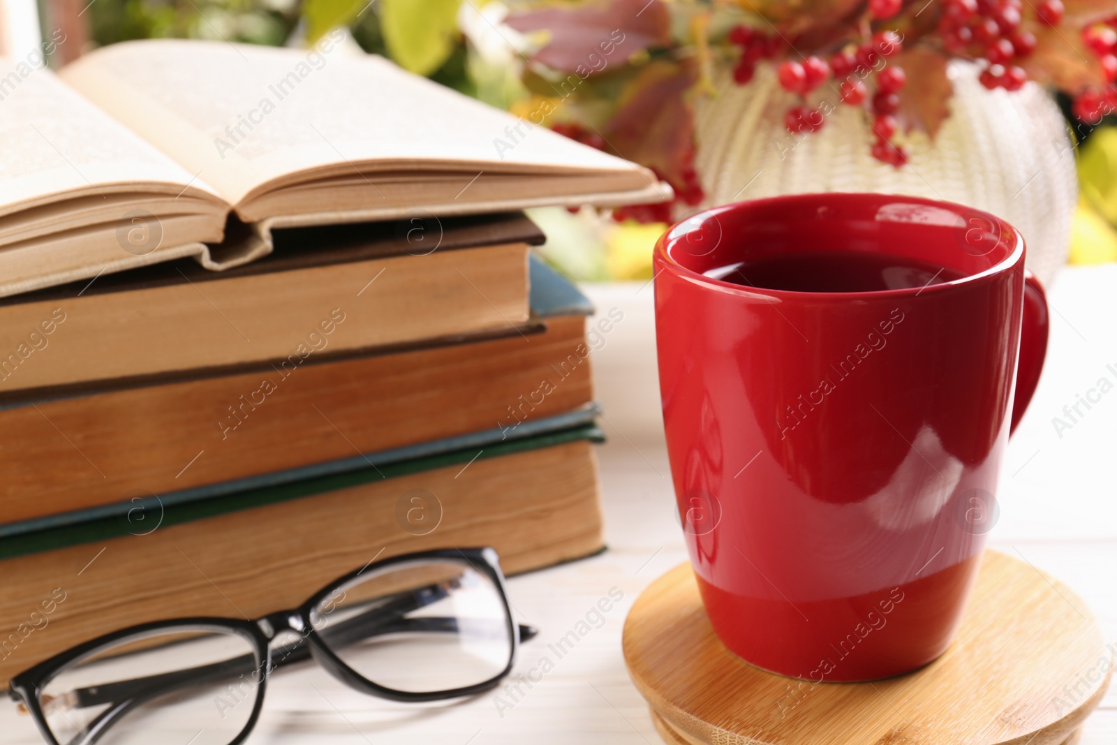 Photo of Cup with hot drink, stack of books and glasses on white wooden table. Autumn atmosphere