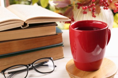 Photo of Cup with hot drink, stack of books and glasses on white wooden table. Autumn atmosphere