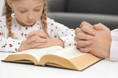Photo of Girl and her godparent praying over Bible together at table indoors, selective focus