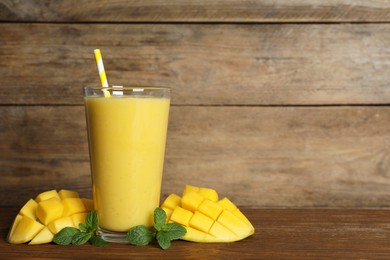 Photo of Glass of tasty smoothie with straw, mint leaves and mango on wooden table. Space for text