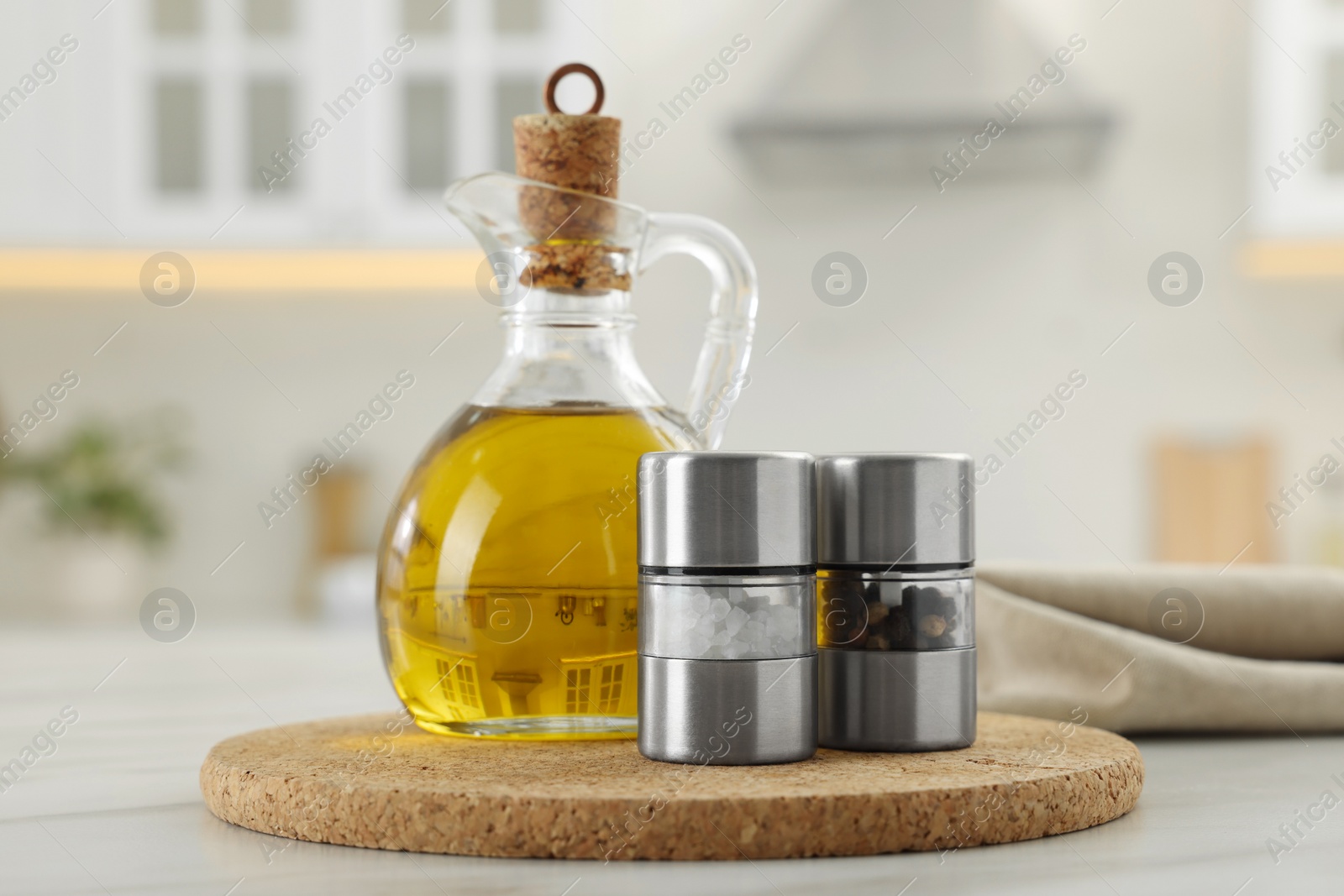 Photo of Salt and pepper mills with bottle of oil on table in kitchen