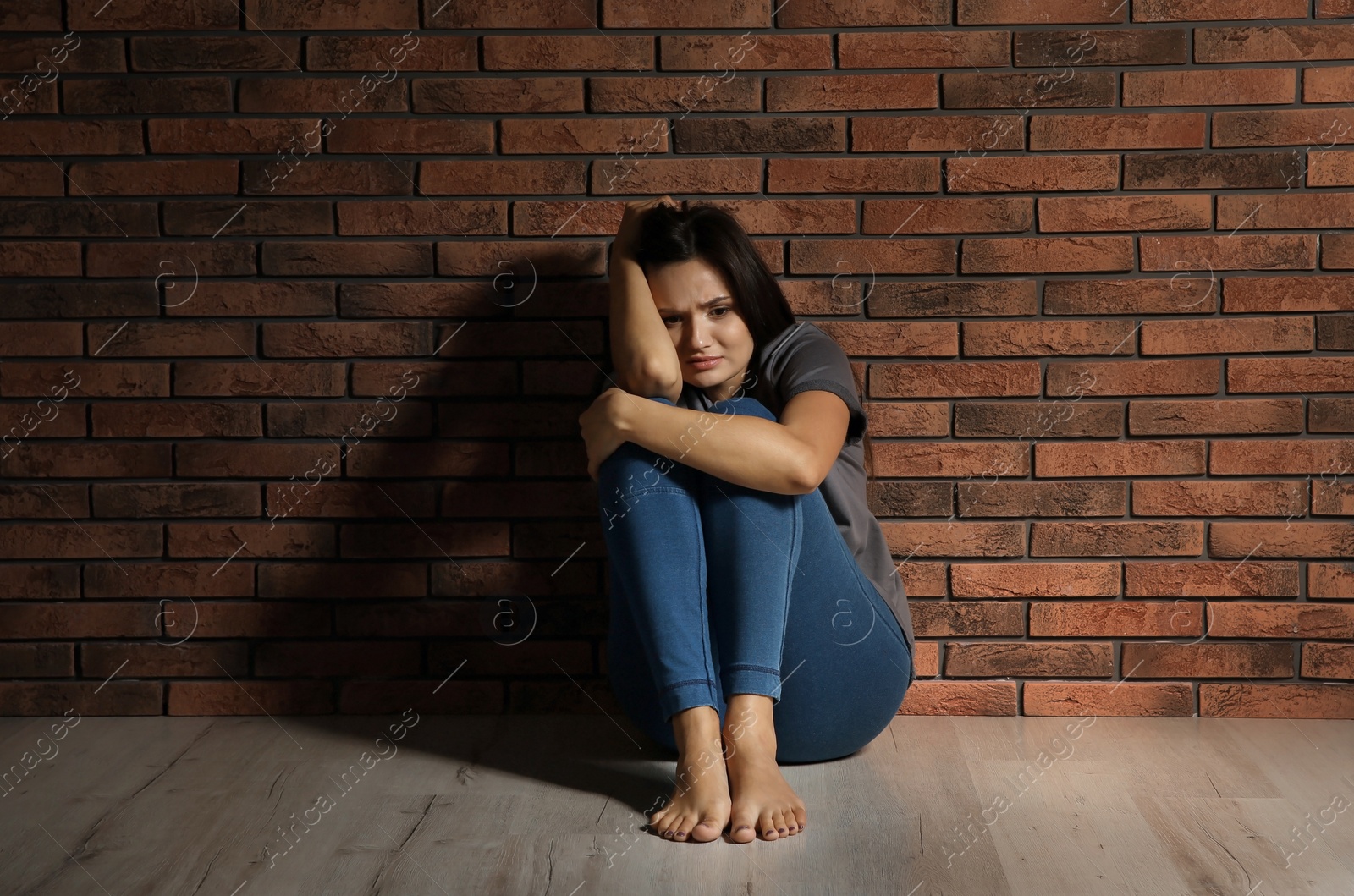 Photo of Depressed young woman sitting on floor near brick wall