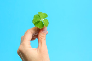 Woman holding beautiful green four leaf clover on light blue background, closeup