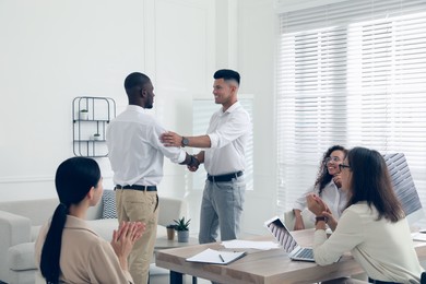 Boss shaking hand with new employee and coworkers applauding in office