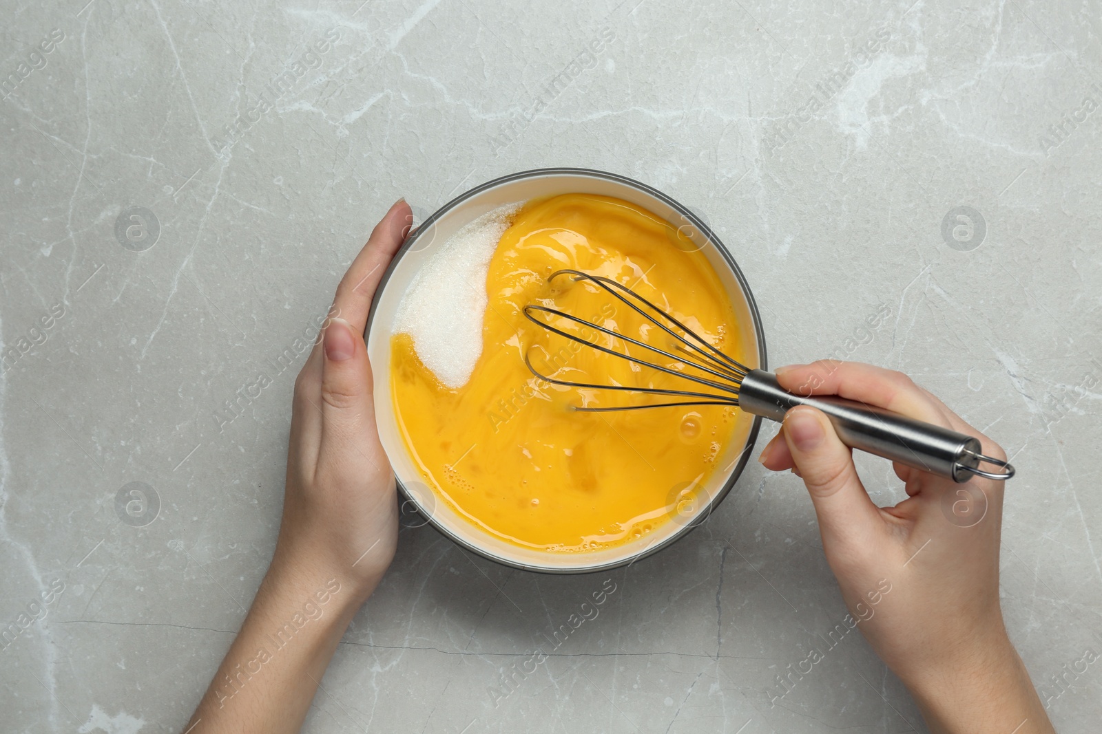 Photo of Woman whisking eggs at light grey table, top view